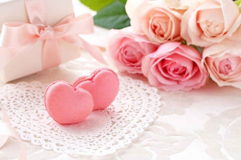 Heart shaped macaroons with Bouquet of pink roses and gift on the table