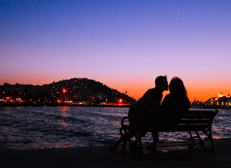 silhouette of young couple kissing on bench in dusk by the sea at Kusadas, Turkey